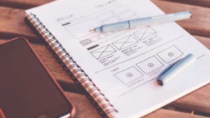 Bocetos de diseño de una página web en un cuaderno junto a un móvil
